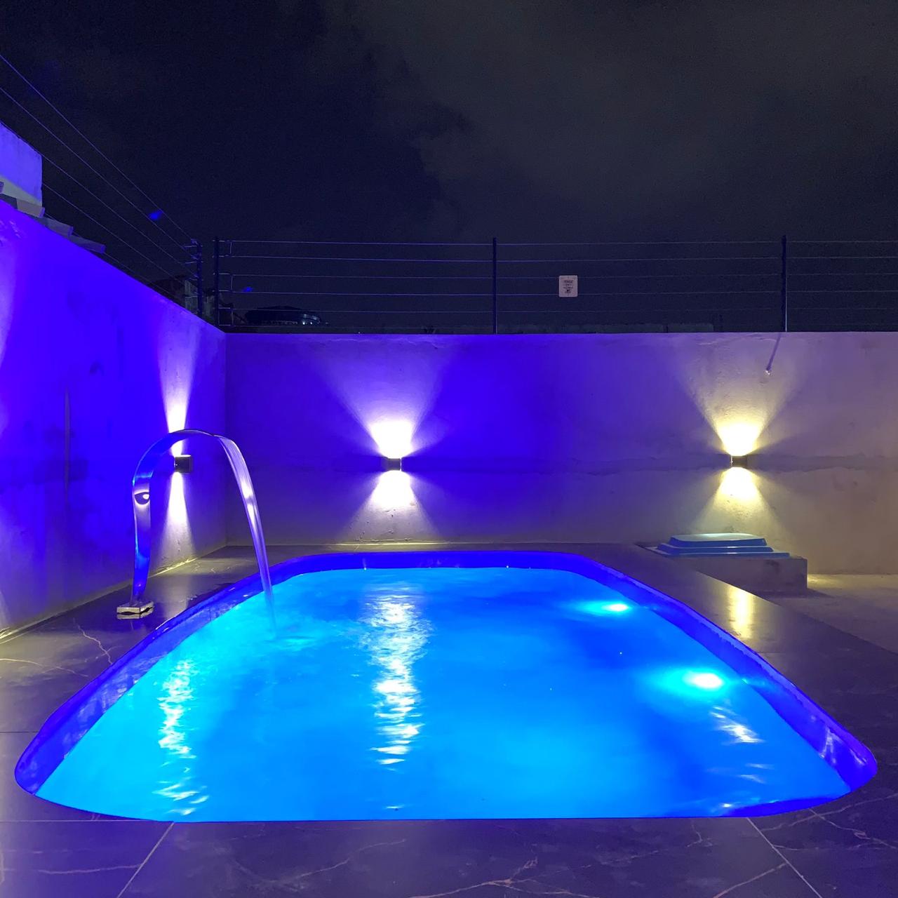 Piscina com queda d'água em arco e deck em porcelanato amadeirado